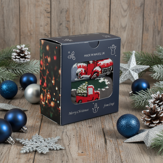 A Men's 2-Pair Christmas Truck Gift Box with a Christmas tree and truck design, placed near a golden Christmas ornament on a grey surface.