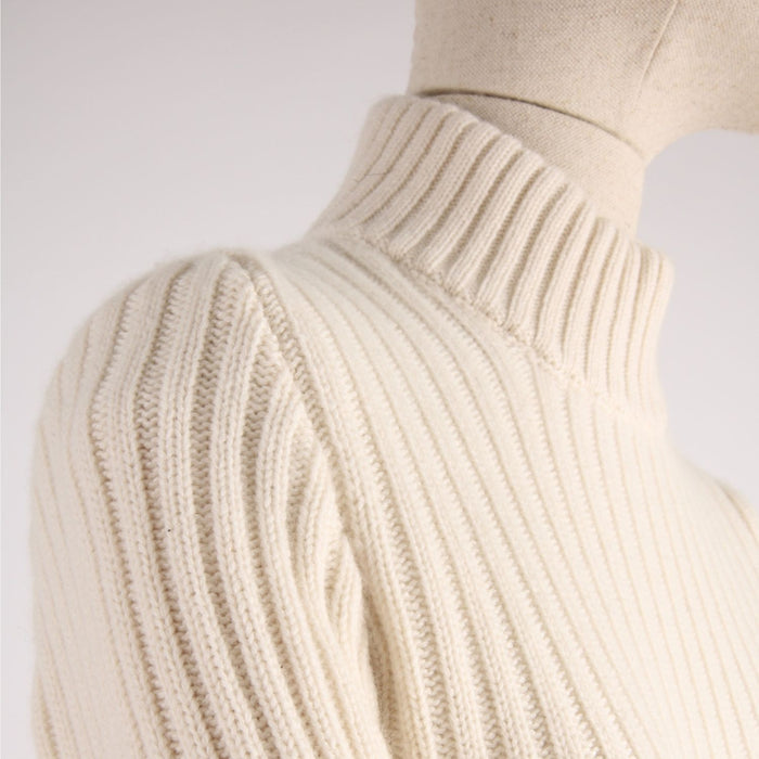 Close-up of a white ribbed sweater on a mannequin against a light background showing the shoulder detail
