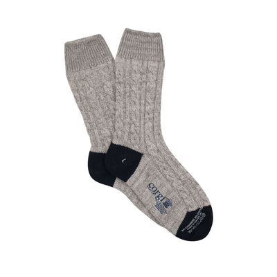 A pair of hand-knitted gray cable cashmere and cotton socks with the brand 'Corgi' visible.