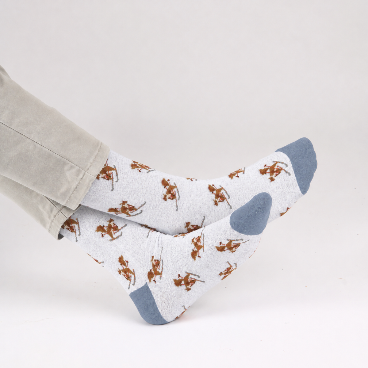 White crew socks with a skiing squirrels pattern, featuring blue heels and toes, worn on feet with light gray pants against a plain white background.