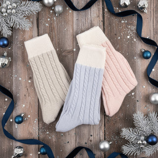 Three pairs of knitted socks in beige, light blue, and pink on a white background
