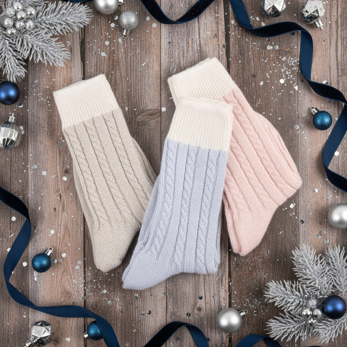 Three pairs of knitted socks in beige, light blue, and pink on a white background