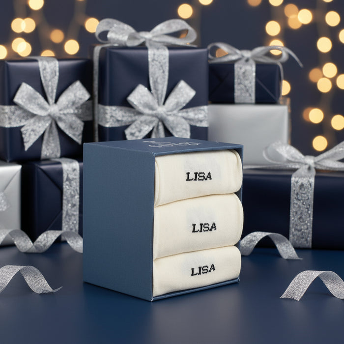 Three folded personalized socks with the name 'LISA' knitted on the side, displayed on a wooden surface.