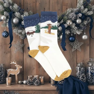 A pair of women's socks with a skiing-themed intarsia knitted design featuring a Dachshund on a snowy hilltop, displayed against a sparkling background.