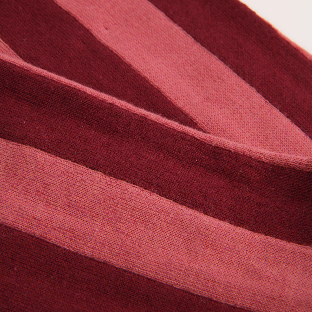 A close-up of a striped knit fabric with alternating wide bands of deep burgundy and muted dusty rose.