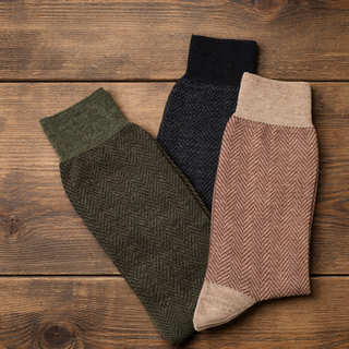 Three pairs of patterned socks in green, black, and beige on a wooden surface.