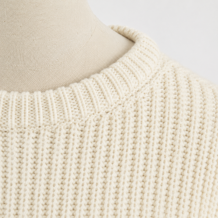 Close-up of a beige knitted sweater on a mannequin with a light gray background