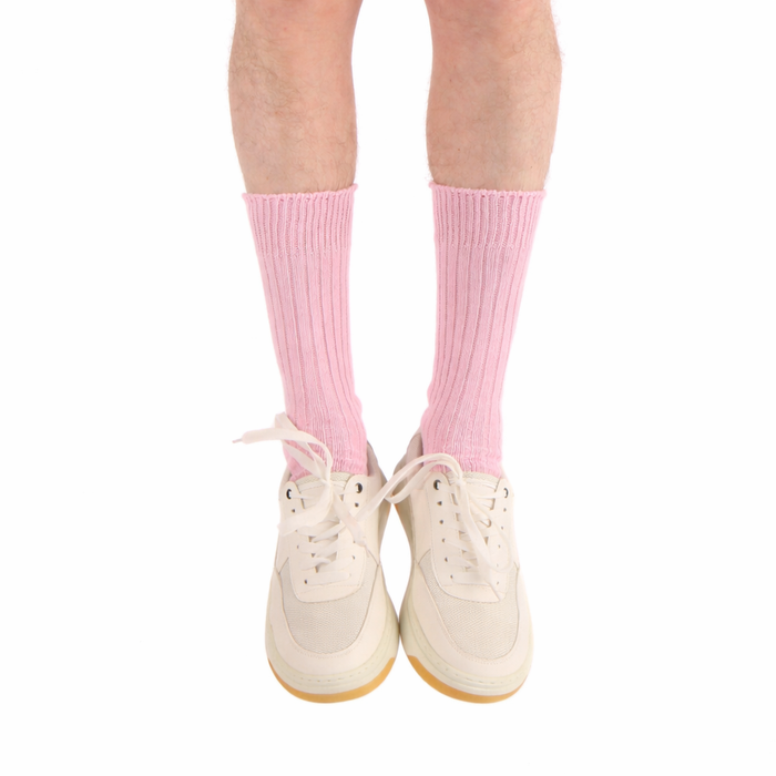 Pink socks worn with white sneakers on a white background