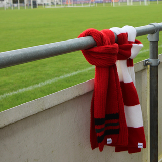 Red and white striped scarf tied to a metal railing with a football field in the background
