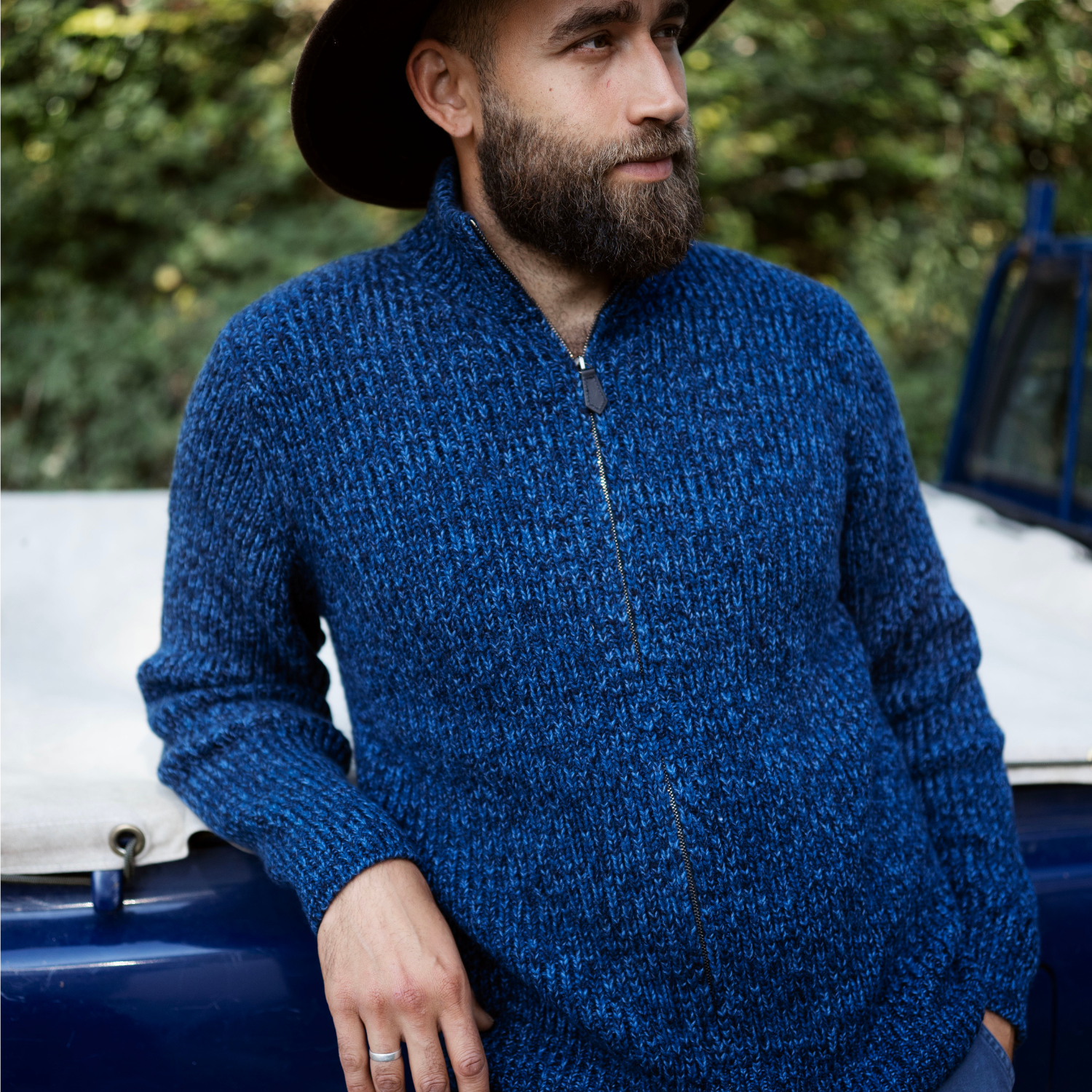 Man wearing a blue sweater standing next to a vintage car with a blurred green background