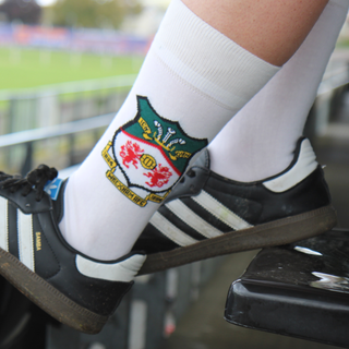 Person wearing white socks with a logo and black Adidas shoes in a stadium setting.