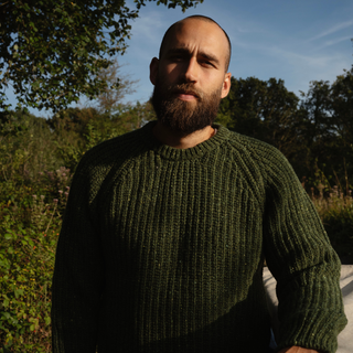 Man wearing a green sweater standing outdoors with trees in the background