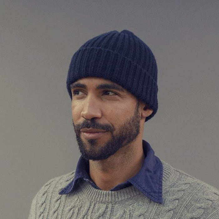 Man wearing a blue knit beanie and gray sweater against a gray background