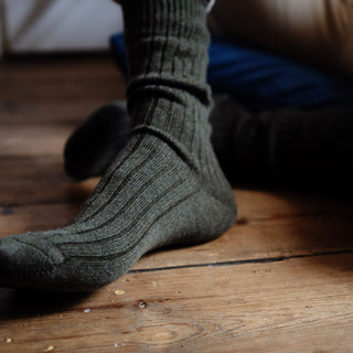 A pair of gray cashmere ribbed men's house socks worn on someone's feet, with the focus on the sock's ribbed design.