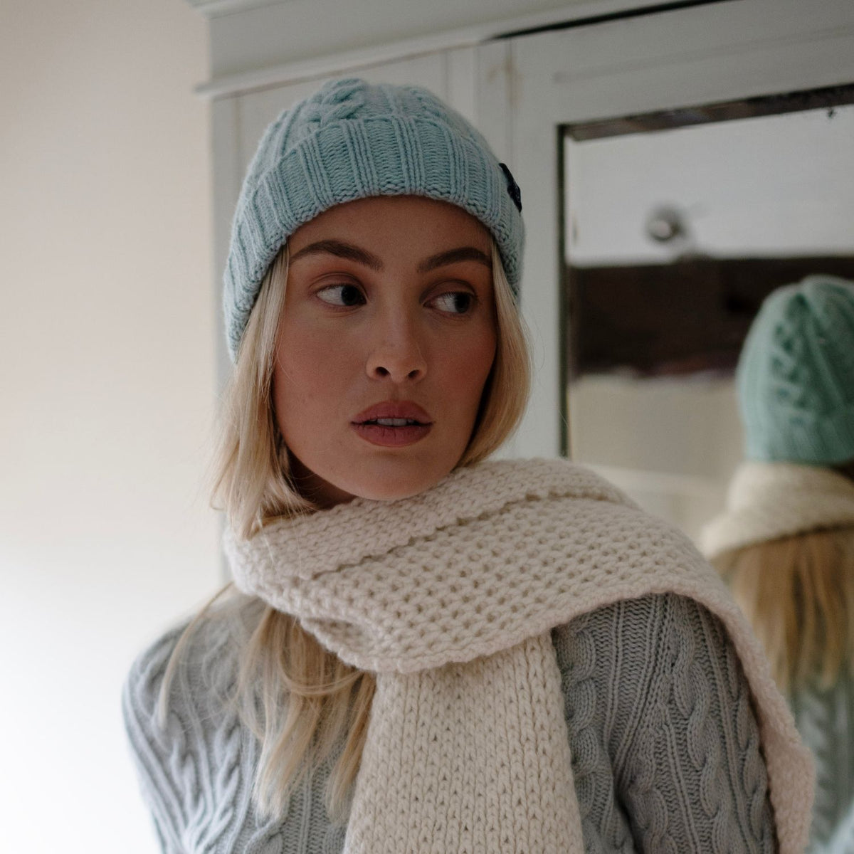 A woman wearing a blue cable wool beanie and a scarf.