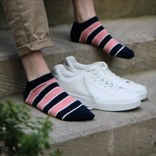A person wearing striped cotton trainer socks in blue and pink colors, paired with a casual outfit and white sneakers.