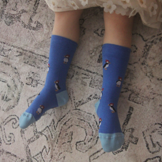 Blue socks with puffin design worn by a child on a patterned carpet