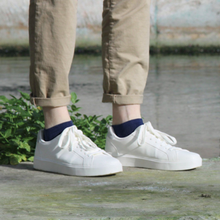 White sneakers with navy socks worn by a person standing on a wooden surface with a natural background.