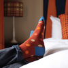 Colorful polka dot socks in a rich rusty red being worn on a bed with a blurred background