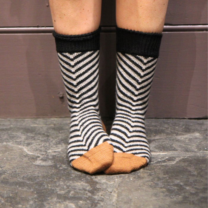 Person wearing black and white striped socks with gold toes on a stone floor.