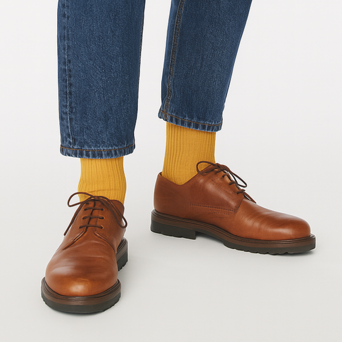 Brown leather shoes worn with blue jeans and yellow socks on a white background
