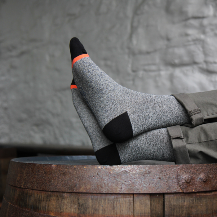 Person wearing gray socks with black and orange accents on a wooden barrel against a stone wall.