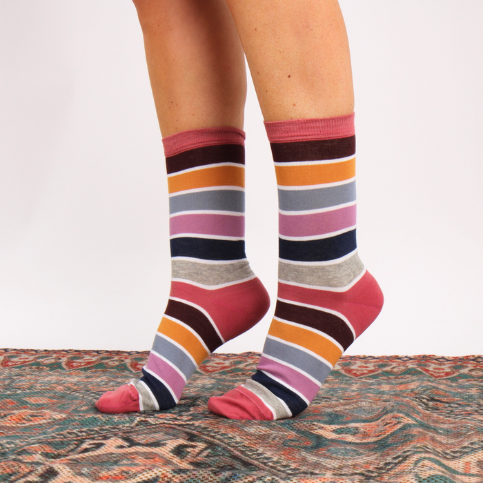 Multicolored striped socks worn by a person on a patterned rug.