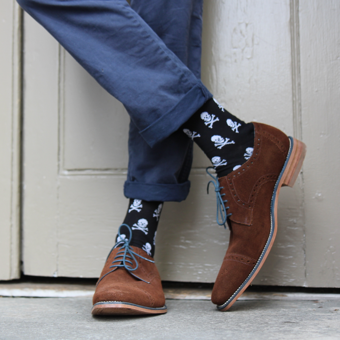 Person wearing brown shoes and black socks with skull patterns against a neutral background