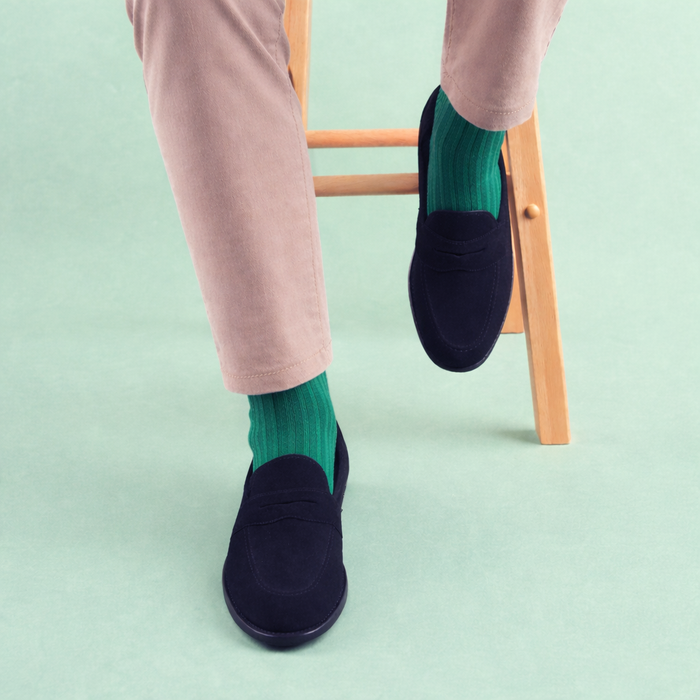 Person wearing navy loafers and green socks on a light green background