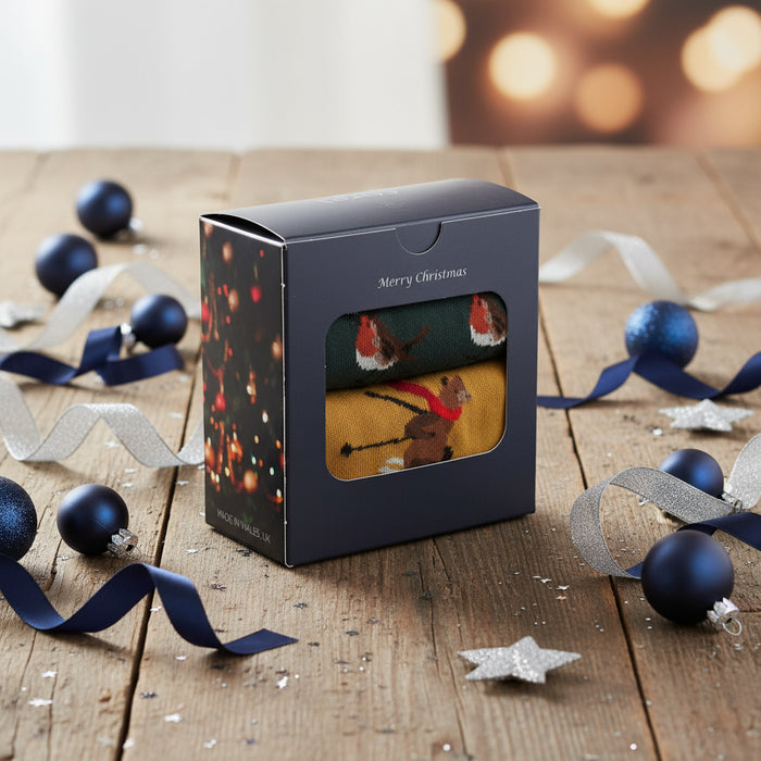 A pair of men's socks with a Christmas-themed design featuring a robin and a bear, packaged in an elegant gift box with 'Merry Christmas' and a festive background.
