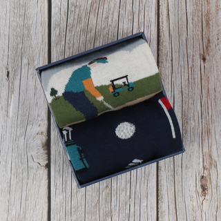 A pair of men's golf socks with a patterned design depicting a golf scene, presented in a gift box.