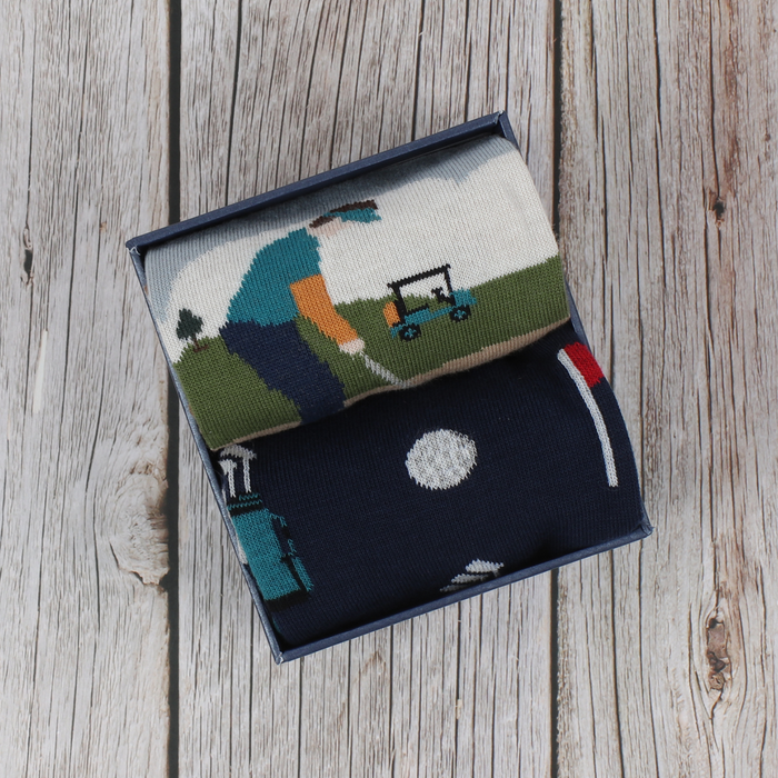 A pair of men's golf socks with a patterned design depicting a golf scene, presented in a gift box.