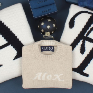 Beige sweater with 'Alex' knitted on it, placed on a dark surface with decorative items.