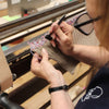 Person working with a loom and yarn, wearing glasses and a dark shirt.
