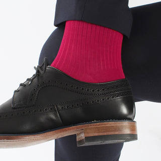 A man's leg wearing a pink ribbed sock, paired with a dark suit and a black shoe.