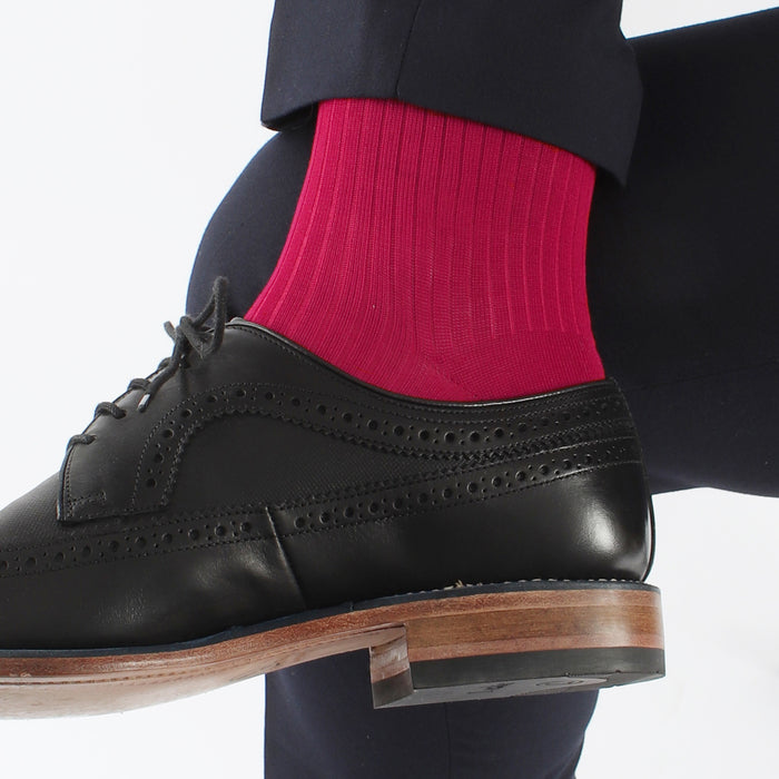 A man's leg wearing a pink ribbed sock, paired with a dark suit and a black shoe.