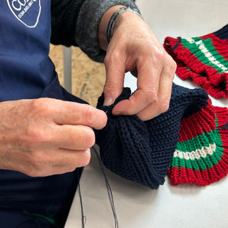 Corgi staff working on the Red Wall beanie hat with a needle and yarn.