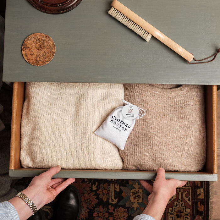 Clothing items in a drawer with a 'Clothes Doctor' bag, on a green surface with a brush.