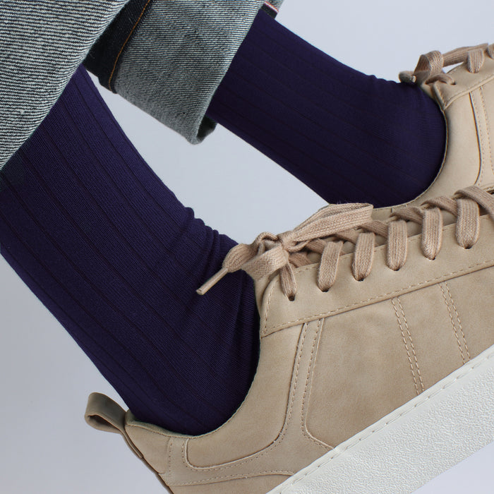Beige sneaker worn with navy socks on a light gray background