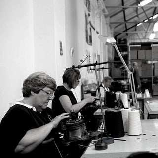 Two women working at a knitting machine in a factory setting.