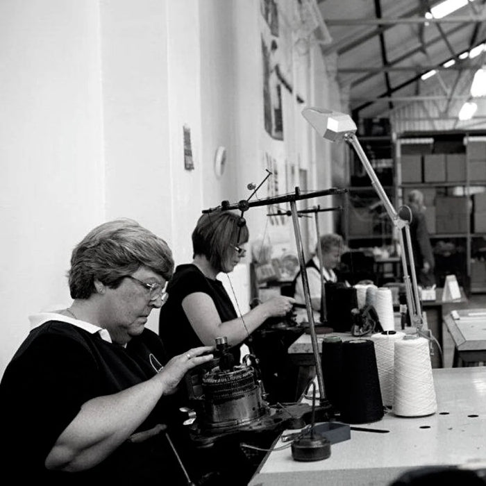 Two women working at a knitting machine in a factory setting.