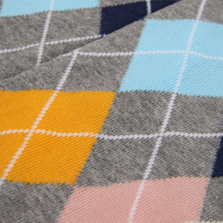Close-up of a colorful classic argyle fabric with orange, pink, blue, and gray diamonds with a white overcheck