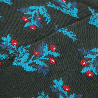 Close-up of a patterned fabric with red and blue holly designs on a green background