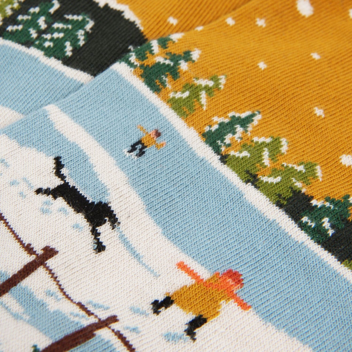 Close-up of a knitted fabric with winter scene design featuring skiers and trees.