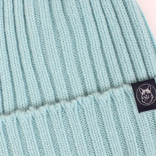 Close-up of a light blue knit beanie with a brand label featuring a Corgi dog logo.