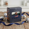 A gift box with a Christmas theme featuring a dachshund design, placed on a wooden surface with holiday decorations in the background.