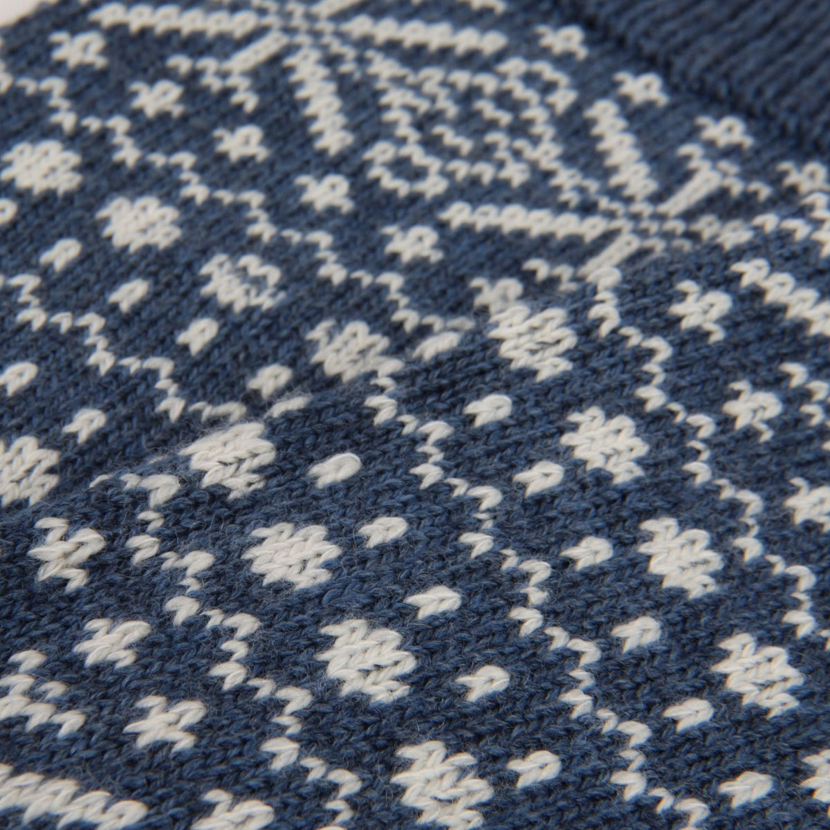 Close-up of a knitted textile with a dark navy blue and off-white Nordic-style pattern.