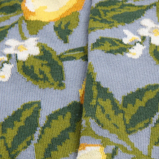 Close-up of a fabric with floral pattern featuring green leaves and white flowers on a blue background.