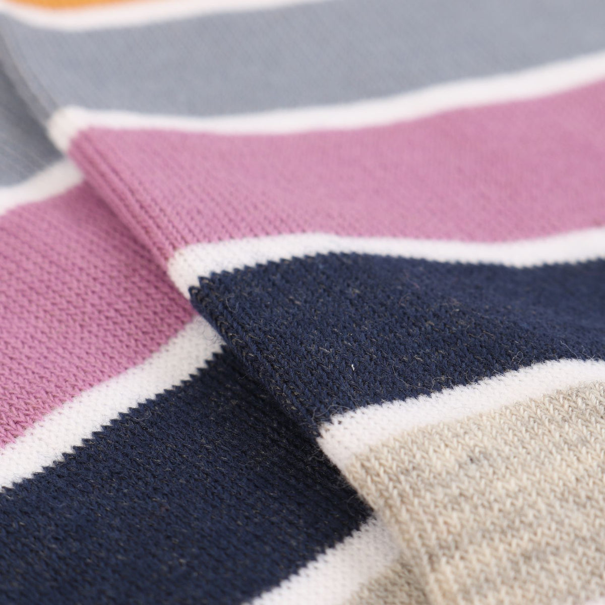Close-up of a knitted fabric with horizontal stripes in dusty pink, navy blue, light gray, and cream.