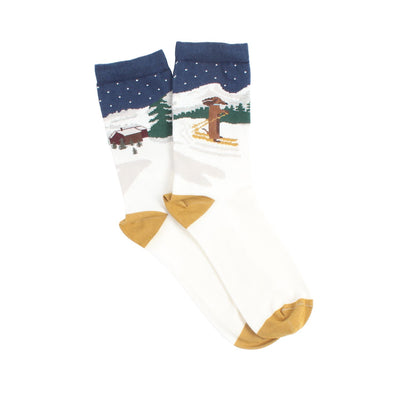 A pair of women's socks with a skiing-themed intarsia knitted design featuring a Dachshund on a snowy hilltop, displayed against a sparkling background.